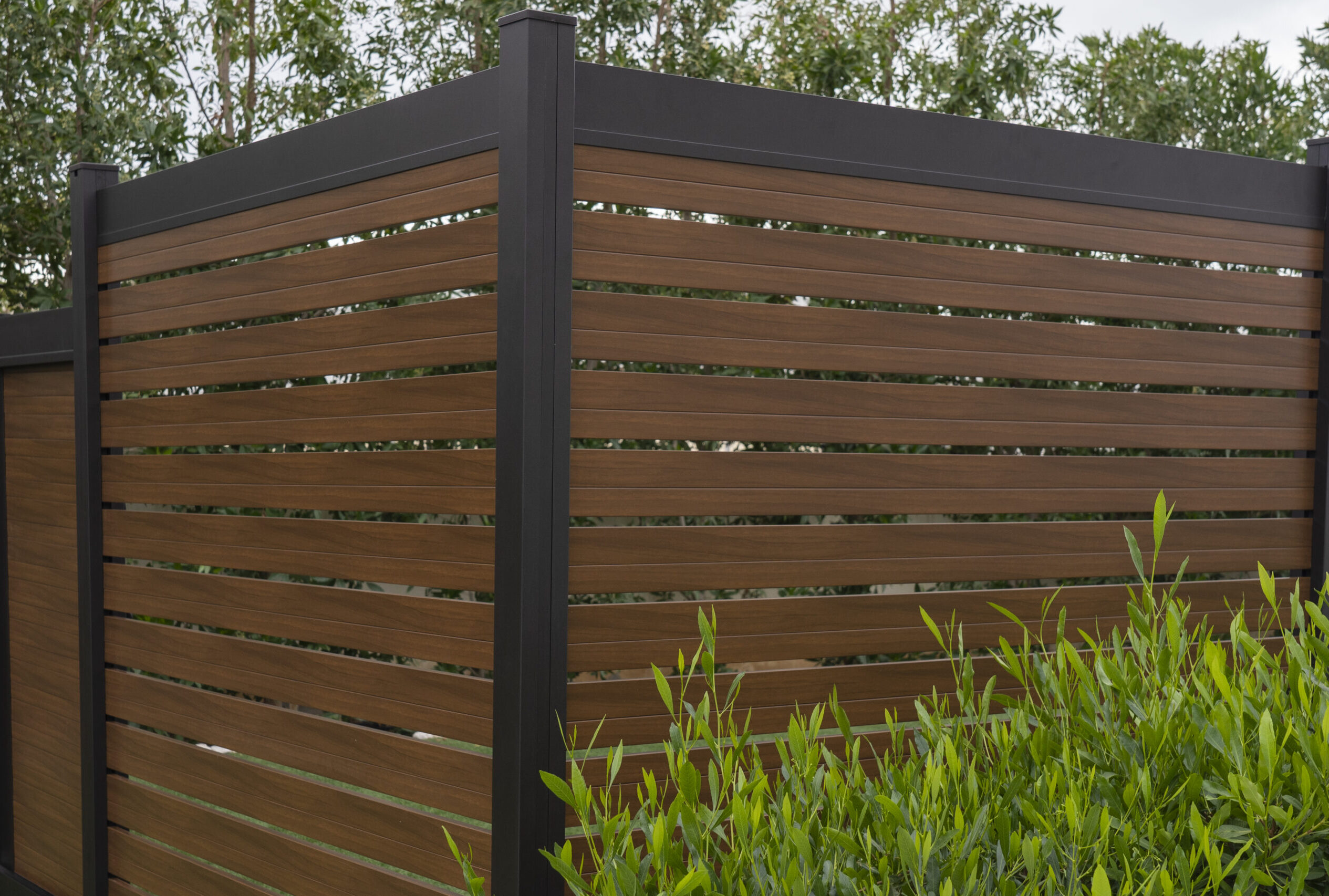 Modern aluminum fence with horizontal brown wood-grain slats installed beside landscaping