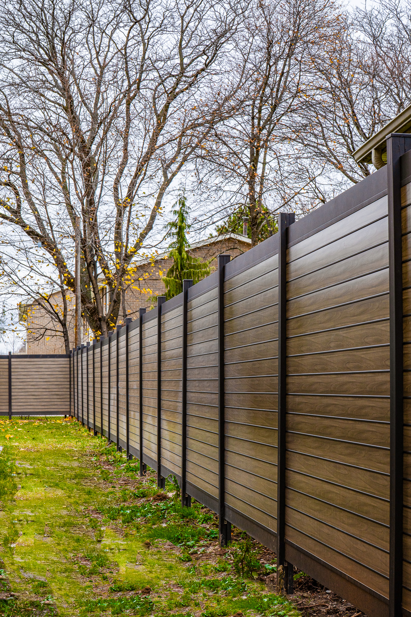 PrimeAlux grey wood-grain aluminum fence run installed along a Canadian residential property - professional fence installation