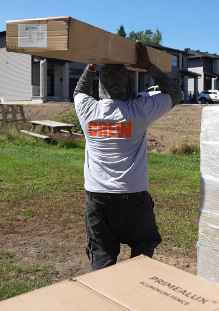 PrimeAlux crew member carrying a boxed aluminum fence panel at a residential construction site