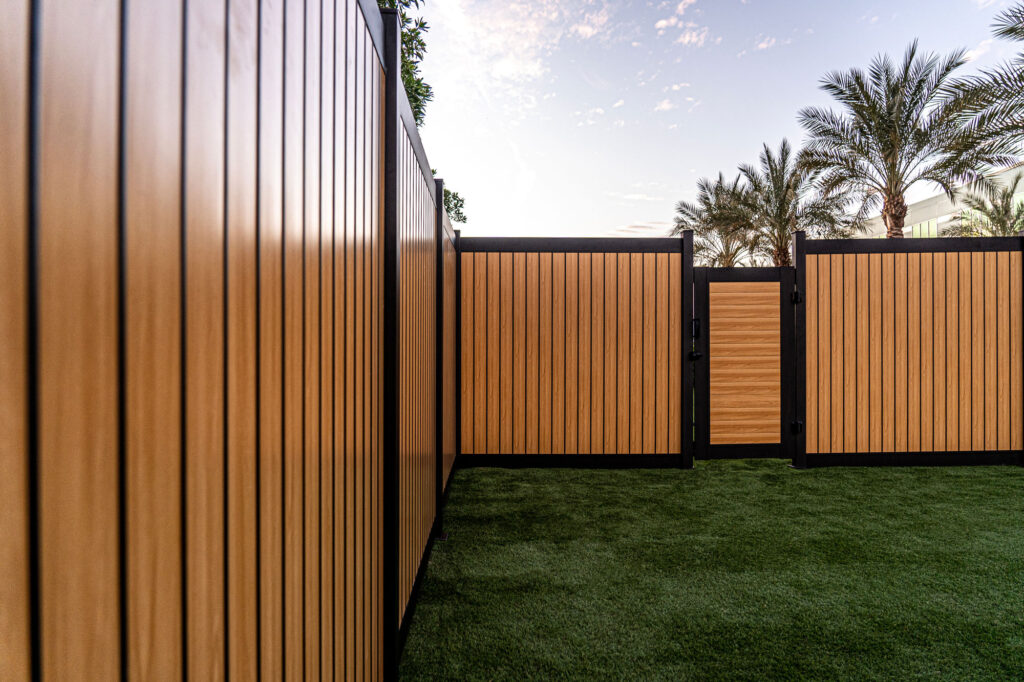 Yellow wood-looking aluminum fence with palm trees in the back
